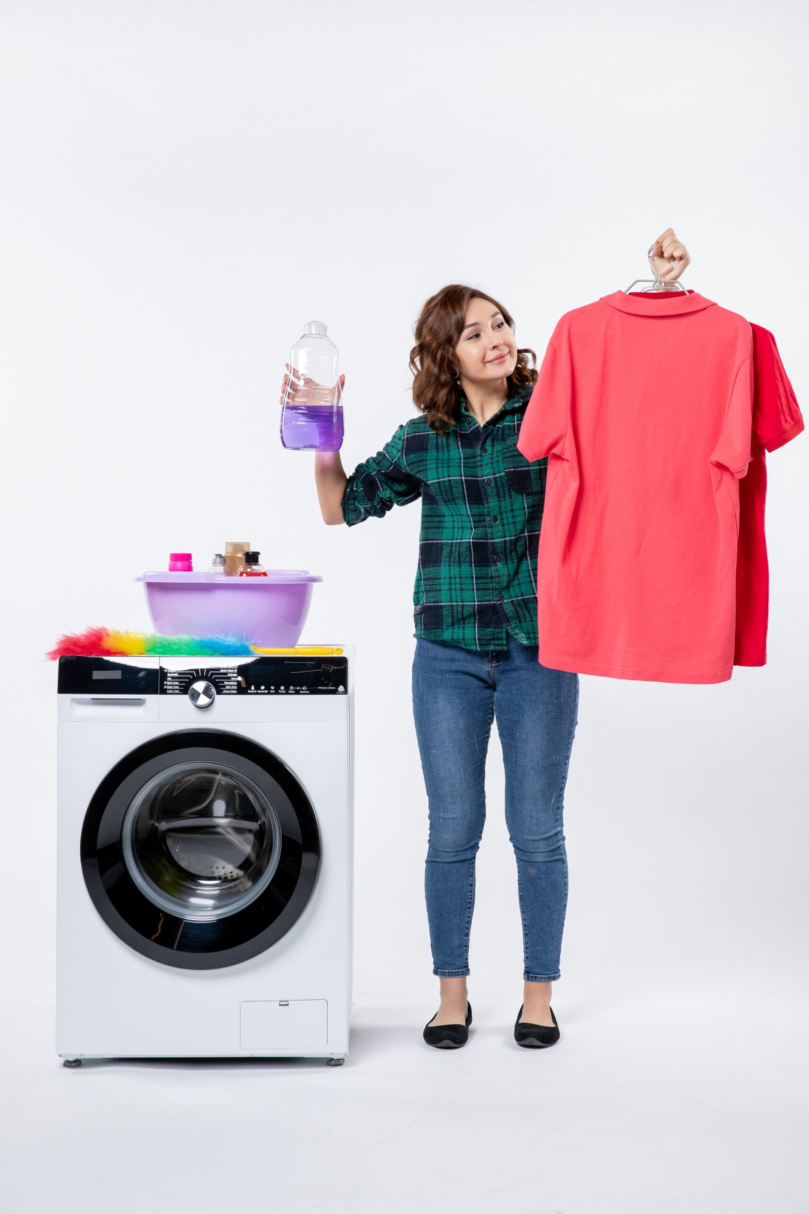 front-view-young-female-holding-clean-clothes-liquid-powder-from-washing-machine-white-wall